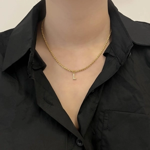 Gros plan sur un collier doré avec un pendentif lettre L scintillant serti de zircons