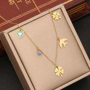 Gold multi-charm necklace with clover, swallow, heart, and evil eye on gold jewelry box
