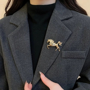 Macro detail of a gold galloping horse brooch with a central diamond on a grey blazer