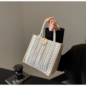 Detail view of a striped linen handbag featuring a wooden button and rope handle design