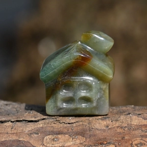 Macro shot of a small hand-carved natural green stone house on a rustic wood base