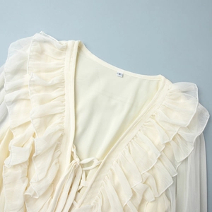 Detail of cream chiffon dress showing V-neck ties, layered ruffles and sheer long sleeves