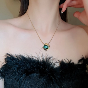 Close-up of a vintage gold chain necklace with a square green gemstone pendant on a model