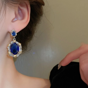 Close-up of vintage gold earrings with oval blue zircons worn by a model