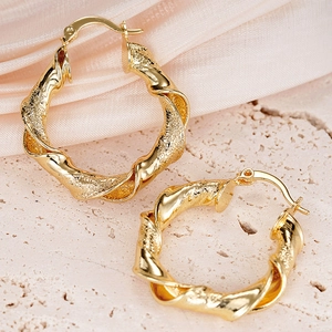 Elegante goldene gedrehte Creolen mit polierter und sandgestrahlter Textur auf Steinfläche