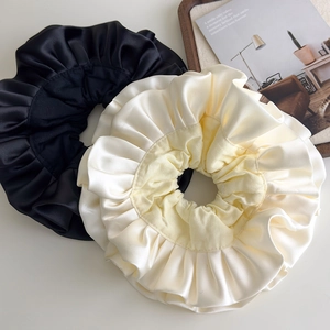 Detailed view of layered satin scrunchies in cream and black colors with ruffles