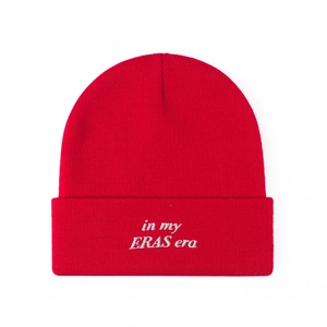 Close-up of red knit beanie featuring white 'in my ERAS era' embroidery on the cuff