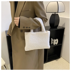 Close-up of white plush faux fur handbag held by model in brown coat for winter fashion