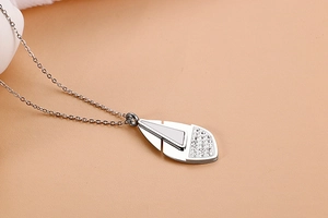 Detail of silver feather pendant necklace with pavé crystals on a peach background