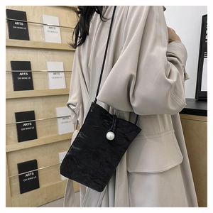 Détail du mini sac bandoulière plissé noir avec fermoir perle porté sur un manteau beige