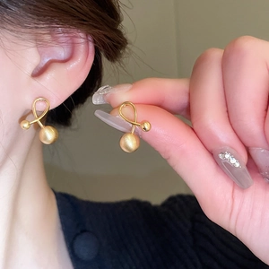 Macro detail of gold plated knotted stud earrings with a dangling matte finish metal ball