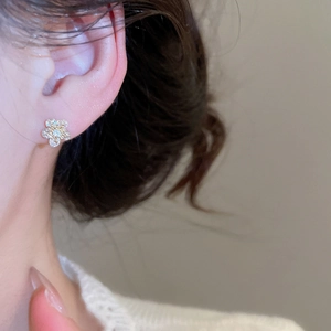 Close-up of golden flower stud earrings with sparkling cubic zirconia on model