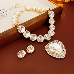 Close-up of gold necklace with heart pendant and matching round crystal earrings on tray