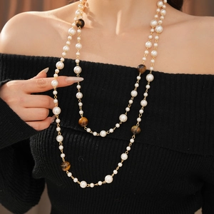 Detail of double-layer necklace with white pearls and brown tiger eye stone beads on a model
