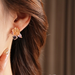 Close-up of elegant flower stud earring with warm orange petals and purple zircon stones