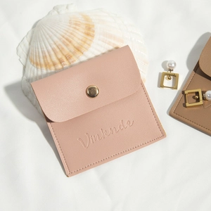 Pink PU leather jewelry pouch with gold snap button on a soft white fabric background
