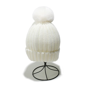 Close-up of white ribbed knit beanie featuring a large faux fur pompom and thick texture