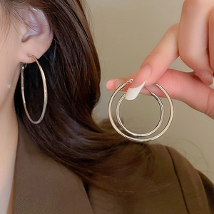 Detail view of large silver hoop earrings worn by a model showing minimalist metal texture