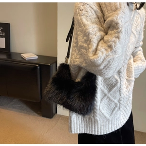 Detail of soft black faux fur shoulder bag worn with a white cable knit sweater