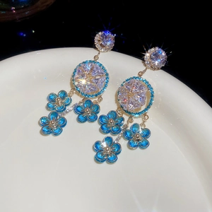 Detailed view of blue floral tassel earrings with zircon studs in a white ceramic dish