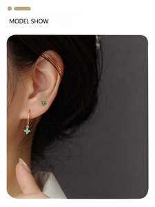 Detail of gold clover earrings with emerald stones shown on a female model