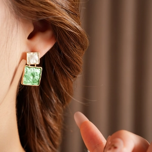 Détail de boucles d'oreilles carrées avec émail vert et blanc sur une base dorée