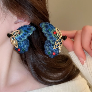 Detailed blue embroidery and metal butterfly earrings shown worn and held