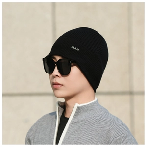 Close-up of black ribbed knit beanie with silver logo emblem and fashion sunglasses