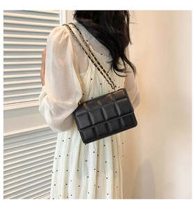 Detail of a black quilted crossbody bag with a leather-woven chain strap on a model