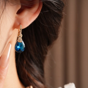 Gros plan d'une boucle d'oreille vintage dorée avec une pierre bleu foncé et des diamants