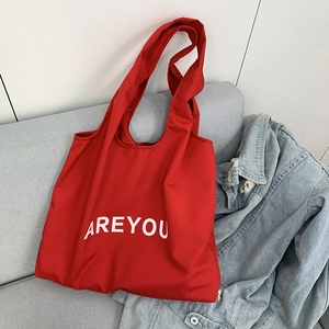 Detail of red canvas tote bag with AREYOU lettering on a stylish grey sofa