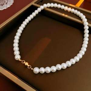 Close-up of elegant white pearl necklace with a gold magnetic clasp on a brown tray