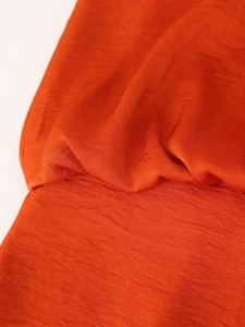 Macro detail of high-quality orange satin fabric with pleated texture and soft gloss