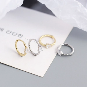 Detail of twisted hoop earrings in gold and silver with pear-shaped cubic zirconia