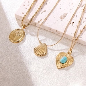 Three gold titanium steel necklaces with shell and heart pendants on stone background