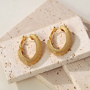 Elegant gold frosted oval hoop earrings with textured finish on minimalist stone background