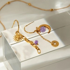 Detail view of gold earrings with sun and moon pendants and purple beads on display