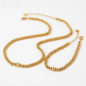 Close-up of golden beaded jewelry set with a single round zircon and lobster clasp