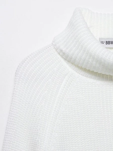 Close-up of white high-neck knit sweater featuring thick ribbed texture and brand neck label