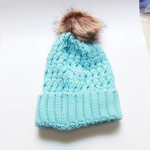 Close-up of bright blue cable knit beanie with fluffy brown faux fur pompom detail