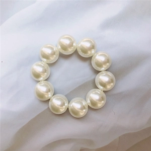 Macro detail of large creamy pearls hair tie on soft white pleated fabric background