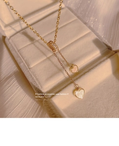 Detailaufnahme der goldenen Doppelherzkette mit weißem Perlmutt in einer Schmuckschatulle
