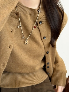Detail of wooden rocking horse pendant on pearl necklace over a camel knit cardigan
