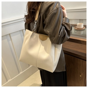Vista a spalla di una borsa tote beige in ecopelle con catena e scritta 'Fashion'