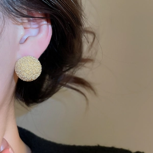 Detail of round golden matte earrings featuring a subtle frosted texture on a female model