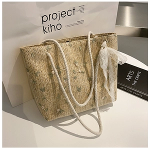 Detail of straw tote bag with green floral embroidery and white lace bow decoration