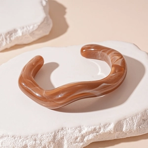 Macro shot of wave-shaped brown acrylic bangle with marble texture on white stone block