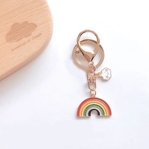 Cute rainbow and smiling cloud enamel keychain with gold hardware on a neutral background