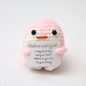 Close-up of pink handmade crochet penguin holding an encouraging English message card