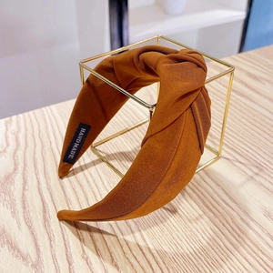 Detail of caramel fabric headband with a stylish knot and handmade tag on a gold stand